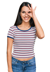 Young hispanic girl wearing casual striped t shirt doing ok gesture with hand smiling, eye looking through fingers with happy face.