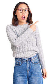 Young beautiful chinese girl wearing casual clothes surprised pointing with finger to the side, open mouth amazed expression.