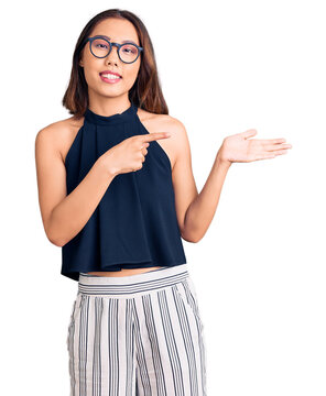 Young beautiful chinese girl wearing casual clothes and glasses amazed and smiling to the camera while presenting with hand and pointing with finger.