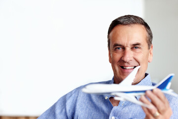 Mature man, portrait and toy plane fly for travel, vacation and holiday planning with a smile at home. Happy, airplane model and retirement of male person with confidence from trip and air traveling