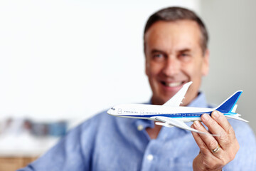 Mature man, flight and toy plane for travel, vacation and holiday planning with a smile at home. Happy, airplane model and retirement of a male person with confidence from trip and air traveling