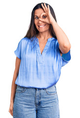 Fototapeta premium Young beautiful brunette woman wearing casual t-shirt smiling happy doing ok sign with hand on eye looking through fingers