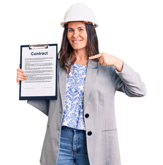 Young beautiful brunette woman wearing architect hardhat holding contract pointing finger to one self smiling happy and proud