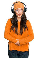 Beautiful brunette young woman listening to music using headphones smiling looking to the side and staring away thinking.
