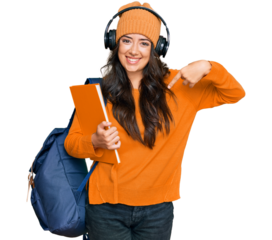 Beautiful brunette young woman wearing student backpack and holding books pointing finger to one self smiling happy and proud