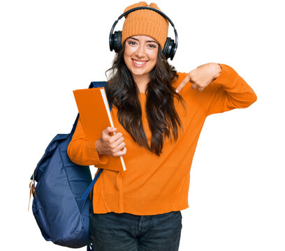 Beautiful brunette young woman wearing student backpack and holding books pointing finger to one self smiling happy and proud
