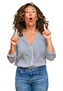 Middle age hispanic woman wearing casual clothes amazed and surprised looking up and pointing with fingers and raised arms.
