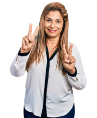 Middle age latin woman wearing business shirt smiling looking to the camera showing fingers doing victory sign. number two.