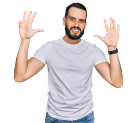 Young man with beard wearing casual white t shirt showing and pointing up with fingers number nine while smiling confident and happy.