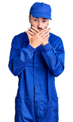 Young hispanic man wearing painter uniform shocked covering mouth with hands for mistake. secret concept.