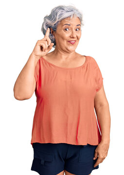 Senior woman with gray hair wearing orange tshirt pointing finger up with successful idea. exited and happy. number one.