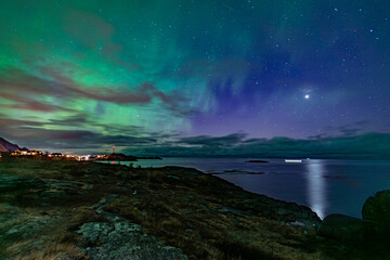 bright majestic northern lights over coast of norway with clouds in the sky and with nothern star reflecting in sea
