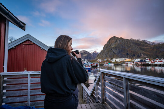 Morning Coffee by the Bay: Woman Enjoying Sørvågen Fisherman Village with Red Houses, Lofoten Islands, Norway