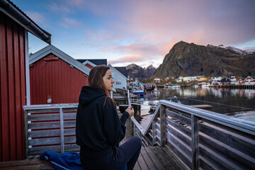 Morning Coffee by the Bay: Woman Enjoying Sørvågen Fisherman Village with Red Houses, Lofoten Islands, Norway