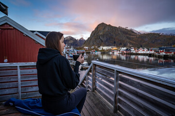 Morning Coffee by the Bay: Woman Enjoying Sørvågen Fisherman Village with Red Houses, Lofoten...