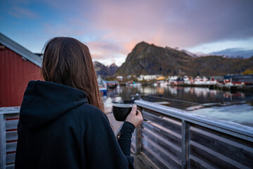 young woman drinking coffee in the morning and taking a look on the bay in Sørvågen fisherman...