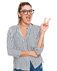 Young caucasian woman wearing business shirt and glasses smiling with happy face winking at the camera doing victory sign. number two.