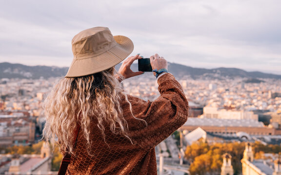 Fototapeta Back view of millennial woman with blank smartphone watching video guide during time for exploring Spanish capital - Barcelona using roaming internet for networking, female generation tracking gps