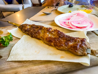 A kebab on a skewer lies on a plate in a restaurant