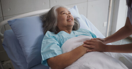 Portrait of Young nurse comforting a senior female patient lying in hospital bed,Caregiver and Lifestyle concept