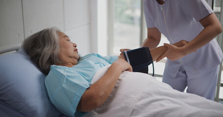 Portrait of Young nurse of an elderly patient measures the patient's blood pressure and heart...