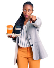 Fototapeta premium Young african american woman wearing business clothes holding take away cup of coffee pointing with finger to the camera and to you, confident gesture looking serious