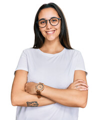 Young hispanic woman wearing casual white t shirt happy face smiling with crossed arms looking at...