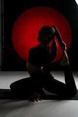 Fototapeta na wymiar Athletic woman doing yoga in the studio and posing against the backdrop of light illuminations in the background. Yoga and meditation concept