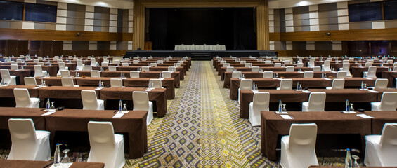 Empty convention center set up with tables, chairs, water, papers and pen for conference, business meeting, training course, lectures or seminars