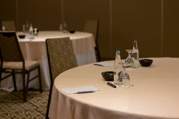 Close up of empty convention center set up with tables, chairs, water, papers and pen for conference, business meeting, training course, lectures or seminars