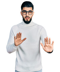 Young arab man with beard wearing elegant turtleneck sweater and glasses moving away hands palms...