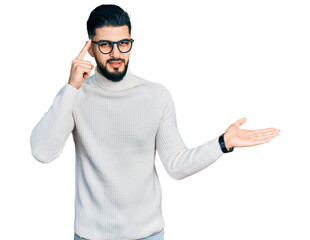 Naklejka premium Young arab man with beard wearing elegant turtleneck sweater and glasses confused and annoyed with open palm showing copy space and pointing finger to forehead. think about it.