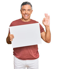 Handsome middle age man holding blank empty banner doing ok sign with fingers, smiling friendly...