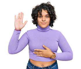 Young hispanic woman with curly hair wearing casual clothes swearing with hand on chest and open...