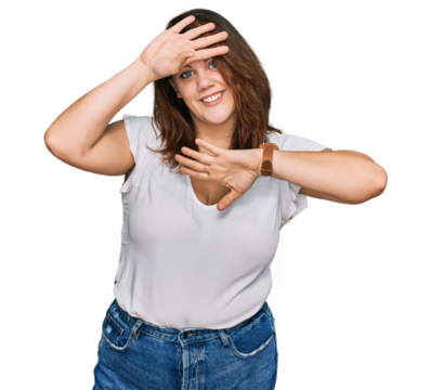 Young plus size woman wearing casual white t shirt smiling cheerful playing peek a boo with hands showing face. surprised and exited
