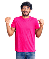 Handsome young man with curly hair and bear wearing casual pink tshirt celebrating surprised and amazed for success with arms raised and open eyes. winner concept.