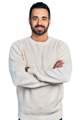 Young hispanic man with beard wearing casual white sweater happy face smiling with crossed arms...
