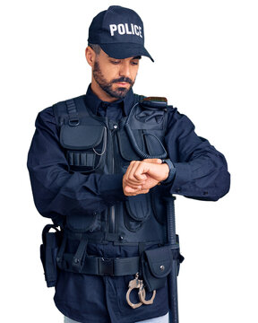 Young hispanic man wearing police uniform checking the time on wrist watch, relaxed and confident