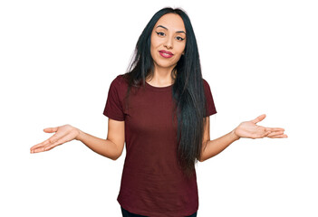 Young hispanic girl wearing casual t shirt clueless and confused expression with arms and hands raised. doubt concept.