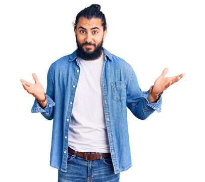 Young arab man wearing casual denim shirt clueless and confused expression with arms and hands raised. doubt concept.