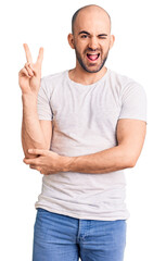 Young handsome man wearing casual t shirt smiling with happy face winking at the camera doing victory sign. number two.