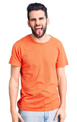 Obraz premium Young handsome man with beard wearing casual t-shirt sticking tongue out happy with funny expression. emotion concept.