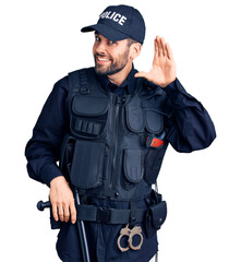 Young handsome man with beard wearing police uniform smiling with hand over ear listening an hearing to rumor or gossip. deafness concept.