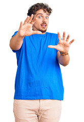 Naklejka premium Young handsome man with curly hair wearing casual clothes afraid and terrified with fear expression stop gesture with hands, shouting in shock. panic concept.