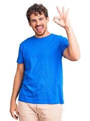 Young handsome man with curly hair wearing casual clothes smiling positive doing ok sign with hand and fingers. successful expression.