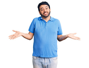 Young hispanic man wearing casual clothes clueless and confused expression with arms and hands...