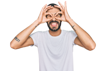 Young hispanic man wearing casual white t shirt doing ok gesture like binoculars sticking tongue out, eyes looking through fingers. crazy expression.