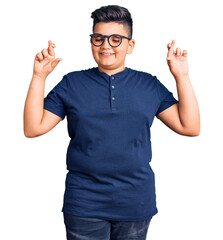 Little boy kid wearing casual clothes and glasses gesturing finger crossed smiling with hope and eyes closed. luck and superstitious concept.