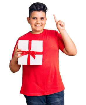 Little boy kid holding gift surprised with an idea or question pointing finger with happy face, number one
