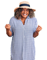Young african american plus size woman wearing summer hat very happy and excited doing winner...